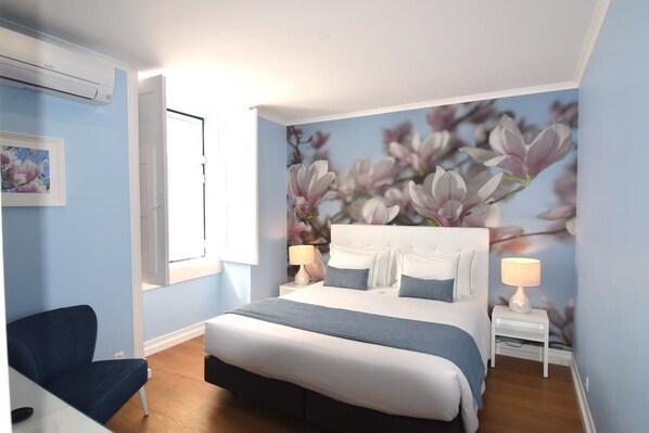 Un dormitorio con una cama, dos mesitas de noche, una silla y un aire acondicionado instalado en la pared.