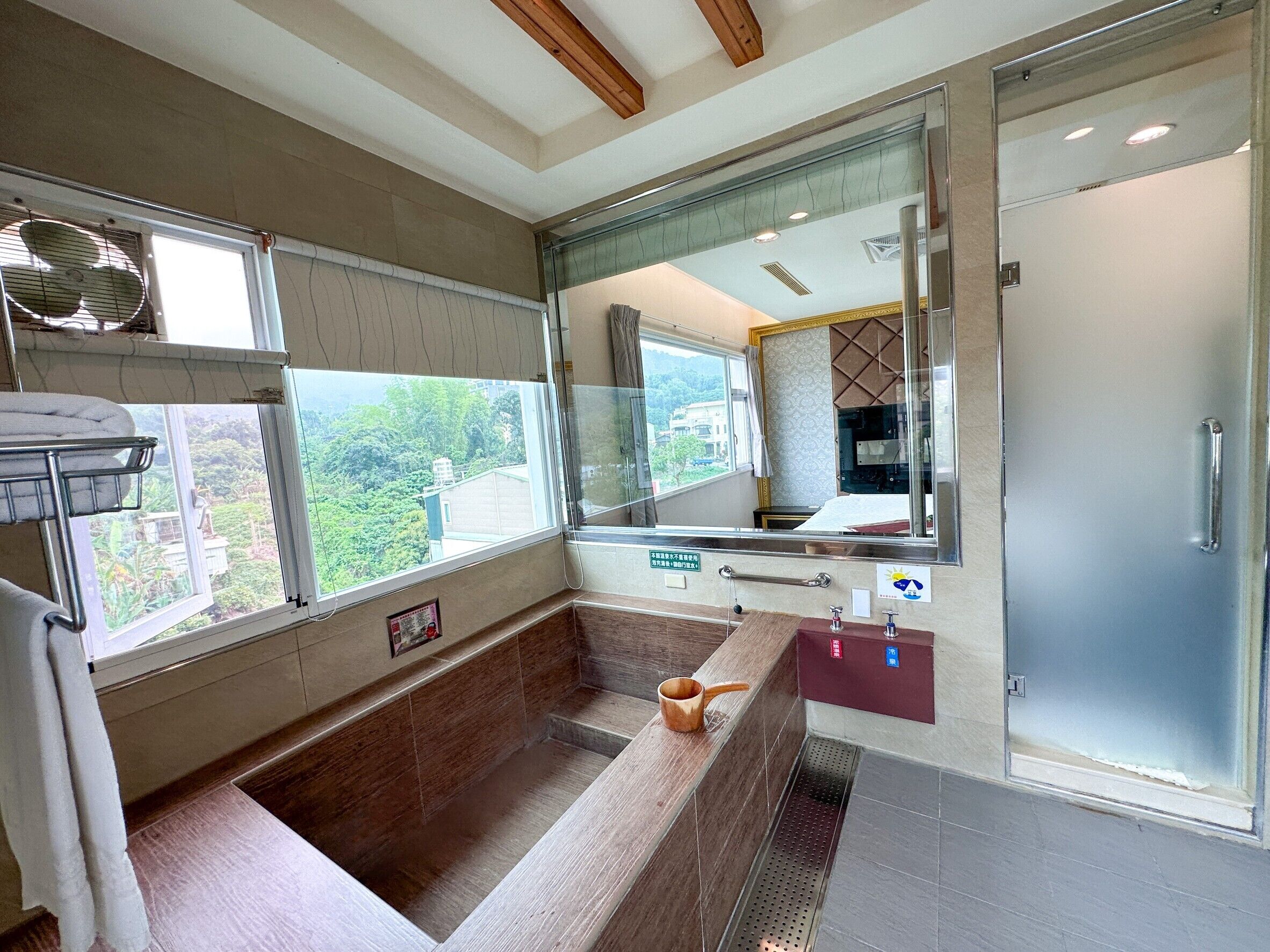 A modern bathroom with a large bathtub, a glass shower enclosure, and a window offering a view of greenery.