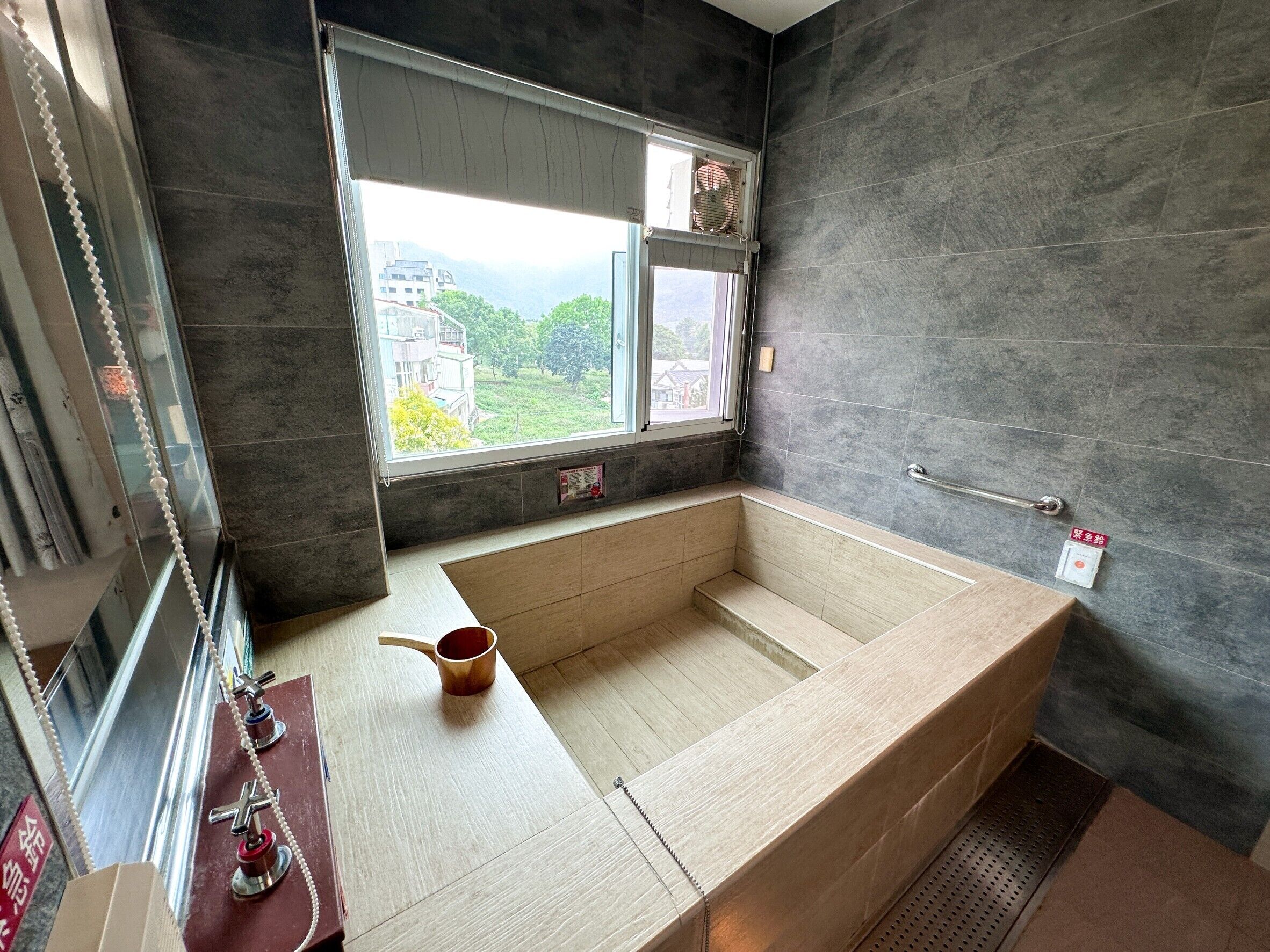 A modern bathroom with a large bathtub, a window with a view of buildings and greenery, and a towel rack.