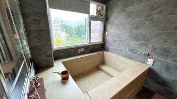 A modern bathroom with a large bathtub, a window with a view of buildings and greenery, and a towel rack.