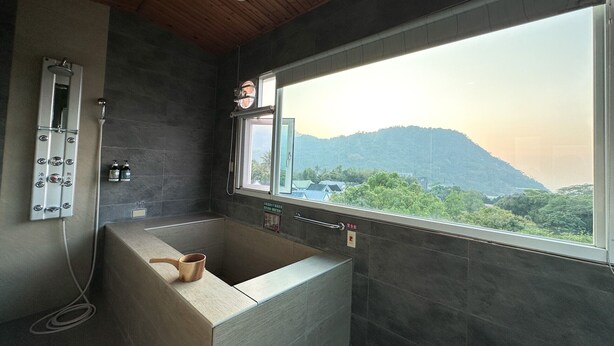 A modern bathroom with a bathtub, a shower, and a large window offering a view of a mountainous landscape. - LiChiuan Hotel Spring Hotel (Tainan)