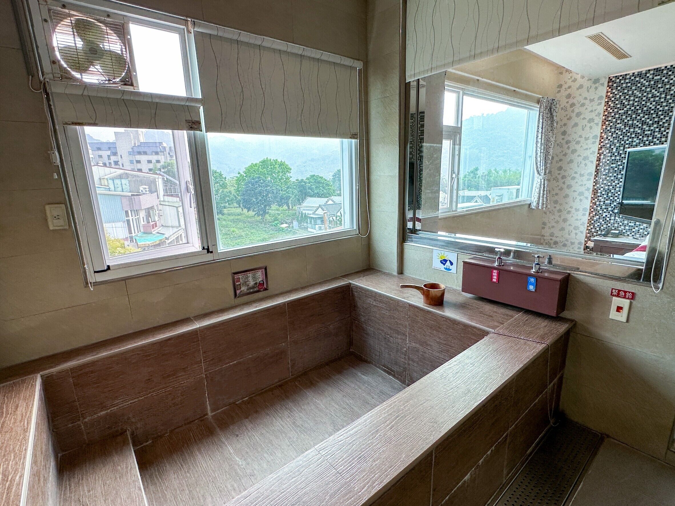 A bathroom with a bathtub, a sink, and a mirror. There is a window with a view of buildings and trees.