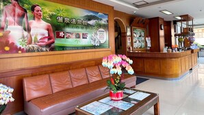 A reception area with a wooden reception desk, a leather sofa, and a large poster advertising a hot spring resort. - LiChiuan Hotel Spring Hotel (Tainan)