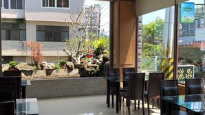 A modern indoor dining area with glass tables and chairs, a stone wall with plants, and a view of buildings and trees outside. - LiChiuan Hotel Spring Hotel (Tainan)