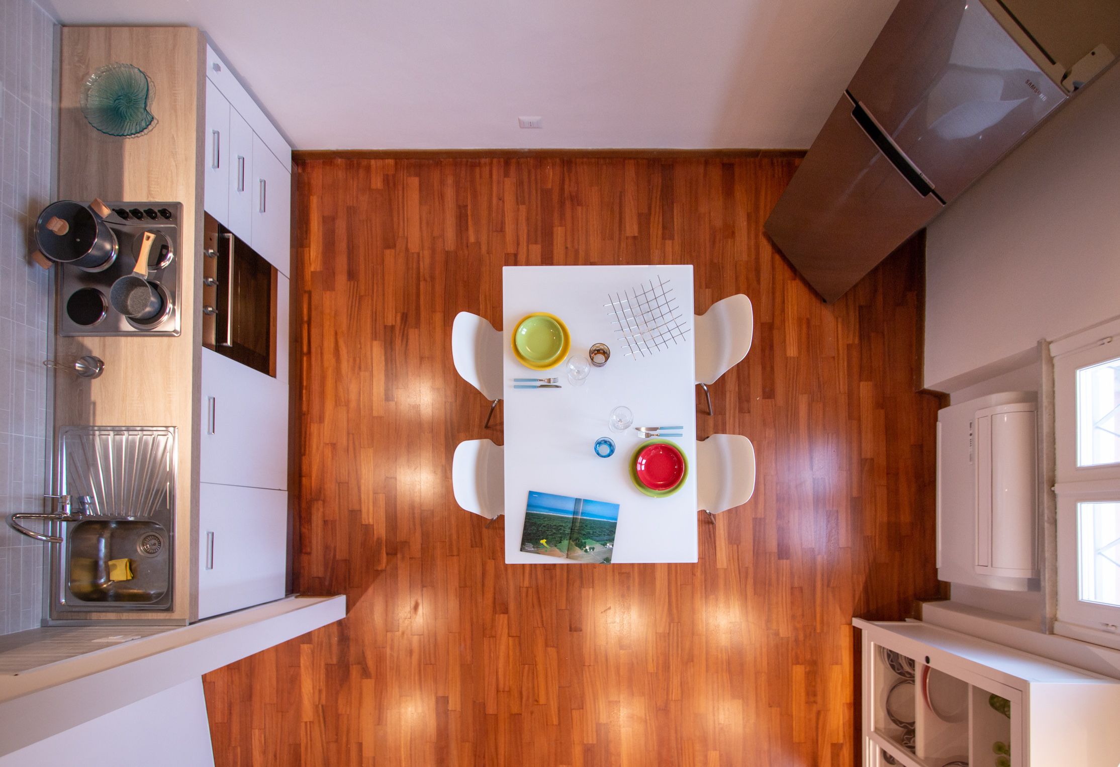 A modern kitchen with wooden flooring, white cabinets, and a white table with a grid pattern.