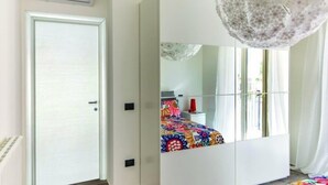 Un dormitorio con un armario blanco, una cama con edredón floral colorido, un espejo grande y una lámpara de araña moderna.