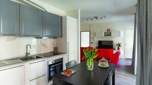 Una cocina moderna con gabinetes grises, encimera negra y un área de comedor con un sofá rojo y un florero con flores.