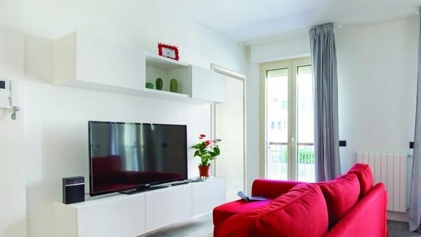 Una sala de estar moderna con un televisor de pantalla plana sobre un mueble blanco, un sofá rojo y una planta en maceta.
