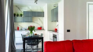 Cocina moderna con armarios grises, comedor con mesa y sillas negras, y un sofá rojo en primer plano.