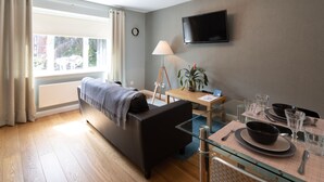 A modern room with a sofa, a dining table set with plates and glasses, a lamp, and a TV on the wall. - Alison Court (Bristol)