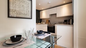A modern kitchen with white cabinets, a black oven, and a dining area with a glass table and metal chairs. - Alison Court (Bristol)