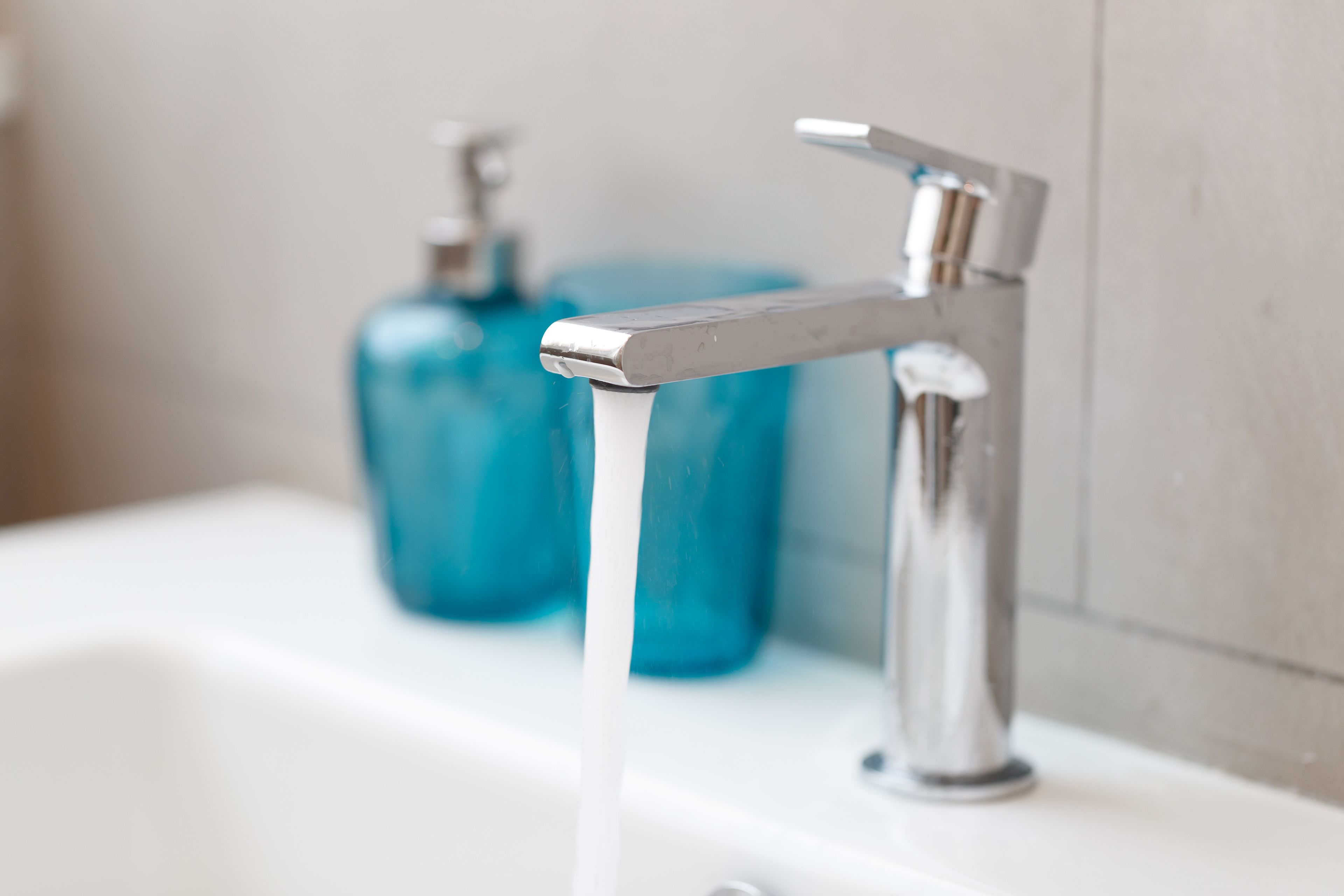 A bathroom with a chrome faucet and a blue soap dispenser.