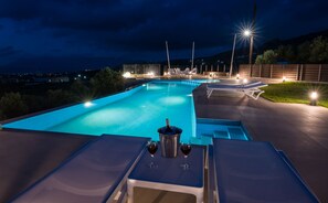 En swimmingpool med udsigt over det omkringliggende landskab, et barområde med en flaske vin og liggestole.
