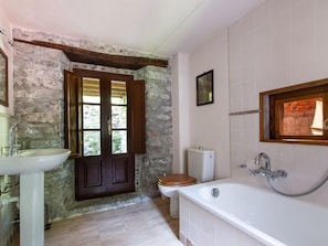 A bathroom with a stone wall, a wooden door, a white sink, a toilet, and a bathtub. - Mulino del Pita (Barga)