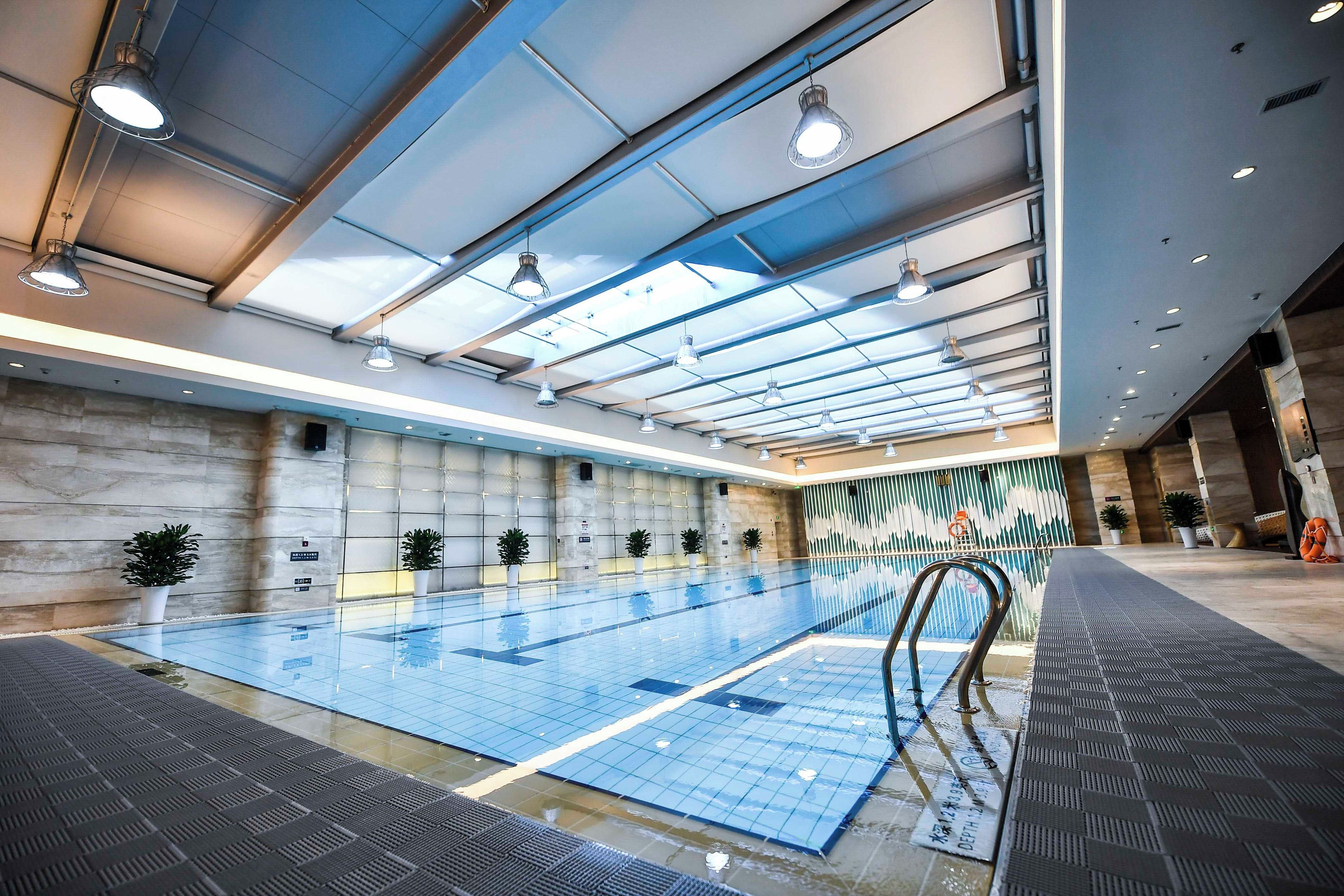 Una piscina con baldosas azul claro, rodeada de paredes con un patrón geométrico y un techo con tragaluces.
