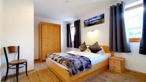 Une chambre à coucher avec un lit en bois, une table de chevet, une chaise, une armoire et un tableau accroché au mur.