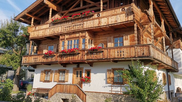 Un chalet traditionnel en bois, doté d’un balcon, de fondations en pierre et de volets en bois.