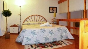 A bedroom with a bed, a nightstand, a lamp, a framed picture on the wall, and a window with blinds.