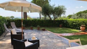 An outdoor patio with stone flooring, a table and chairs, a sun umbrella, and potted plants.
