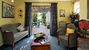 A cozy living room with wicker furniture, a coffee table with fruits, and a view to an outdoor patio. - Be My Guest Lodge (Cape Town)