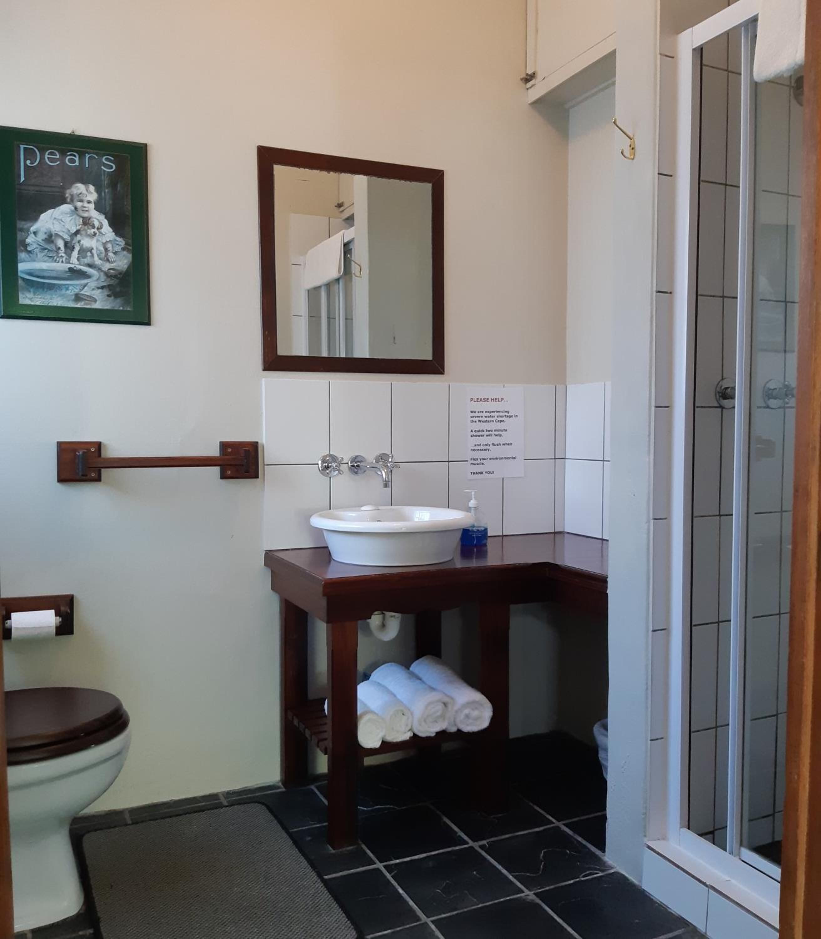 A compact bathroom with a toilet, sink, and shower. A sign requests help for a Western flash shortage.