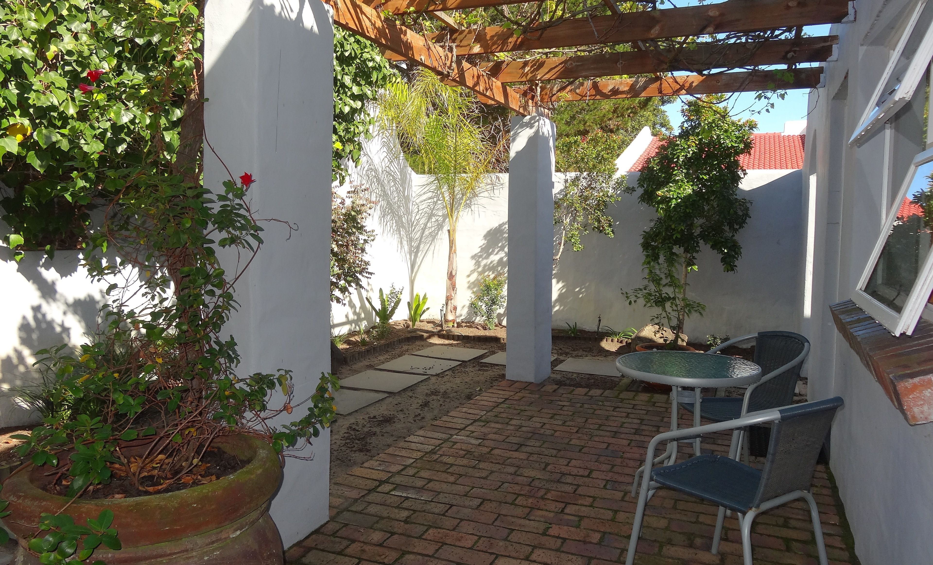 Une terrasse avec un sol en briques, une pergola, une table et des chaises.