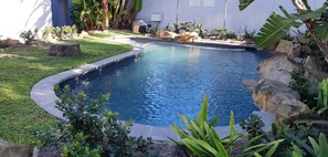 A swimming pool with a curved edge, surrounded by a well-maintained lawn and various plants. - Be My Guest Lodge (Cape Town)