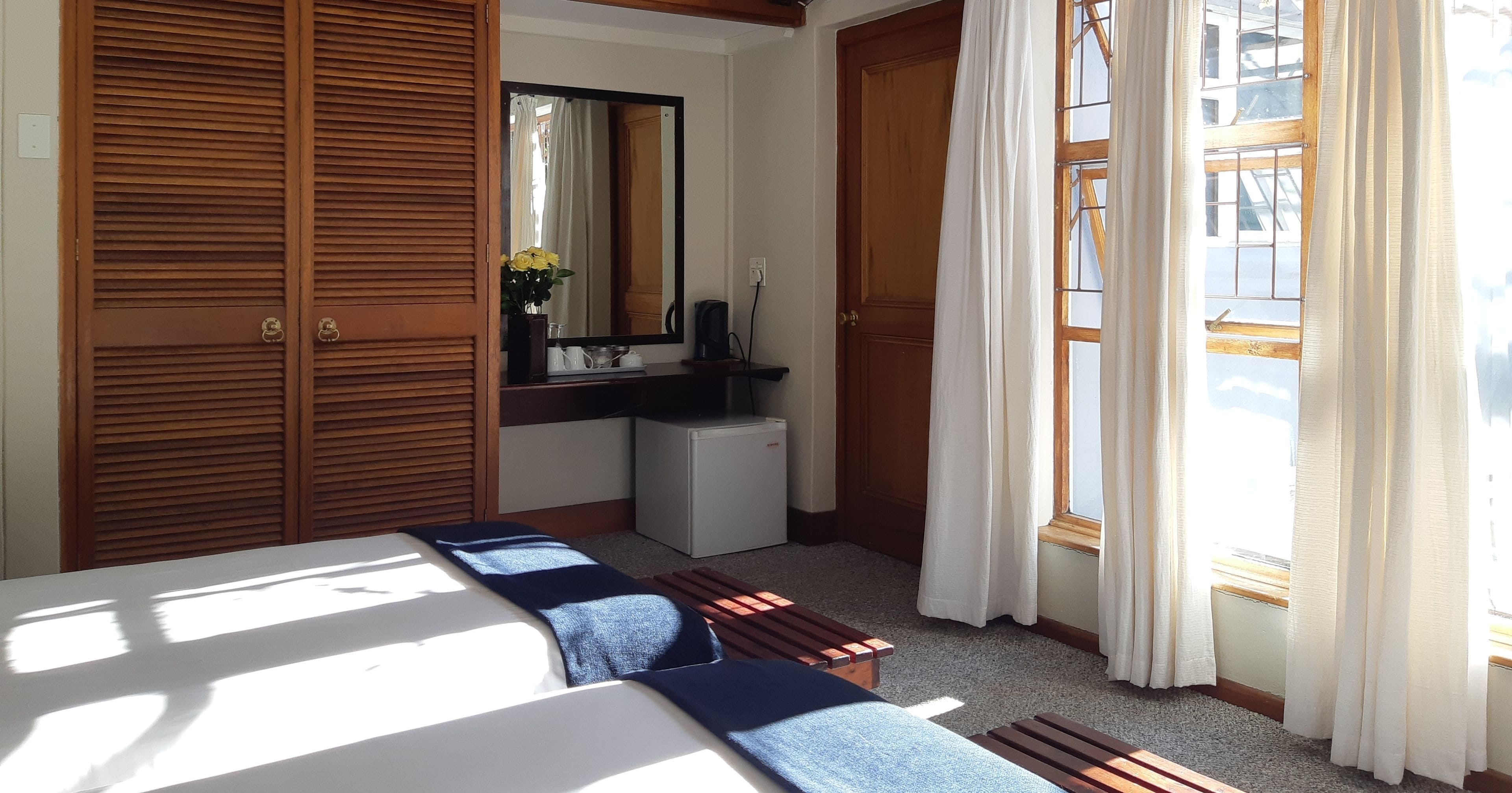 A bedroom with a bed, a small desk, a mirror, and a window with curtains.