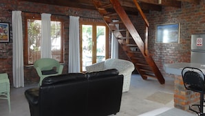 A rustic interior with a brick wall, a wooden staircase, a sofa, a dining area, and a refrigerator. - Be My Guest Lodge (Cape Town)