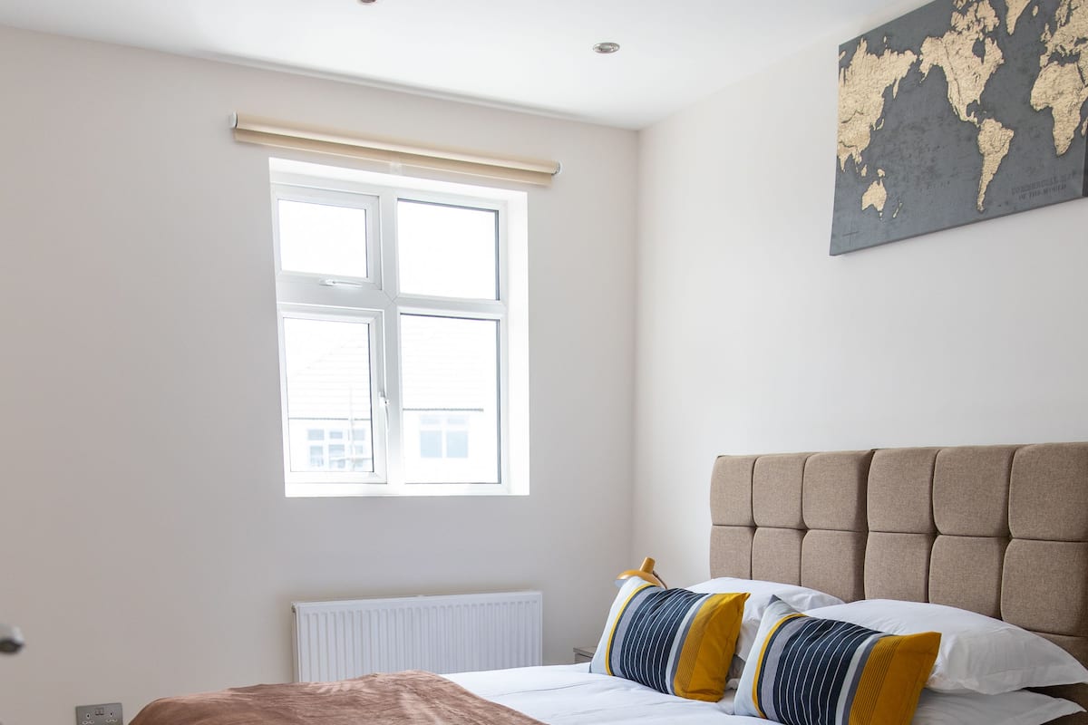 Une chambre avec un grand lit, une fenêtre avec des stores, un radiateur et une carte du monde accrochée au mur.