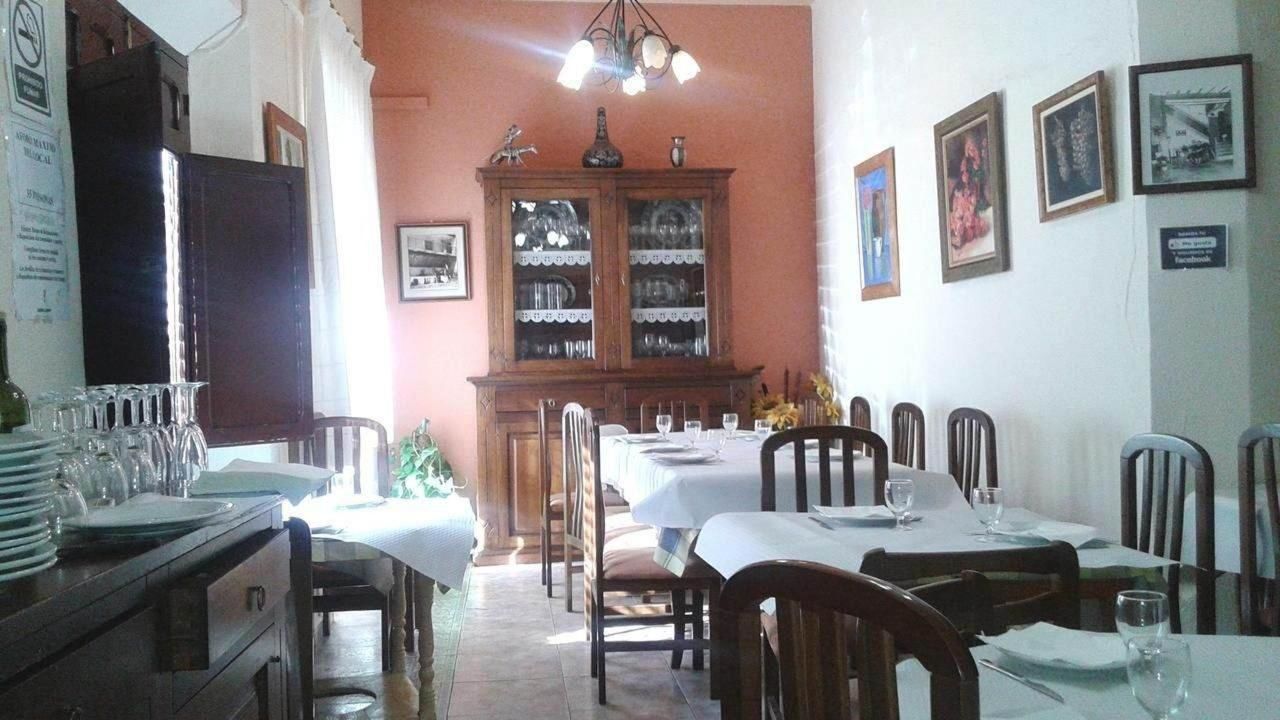 A dining area with multiple tables set for meals, a cabinet with glassware, and framed pictures on the walls.