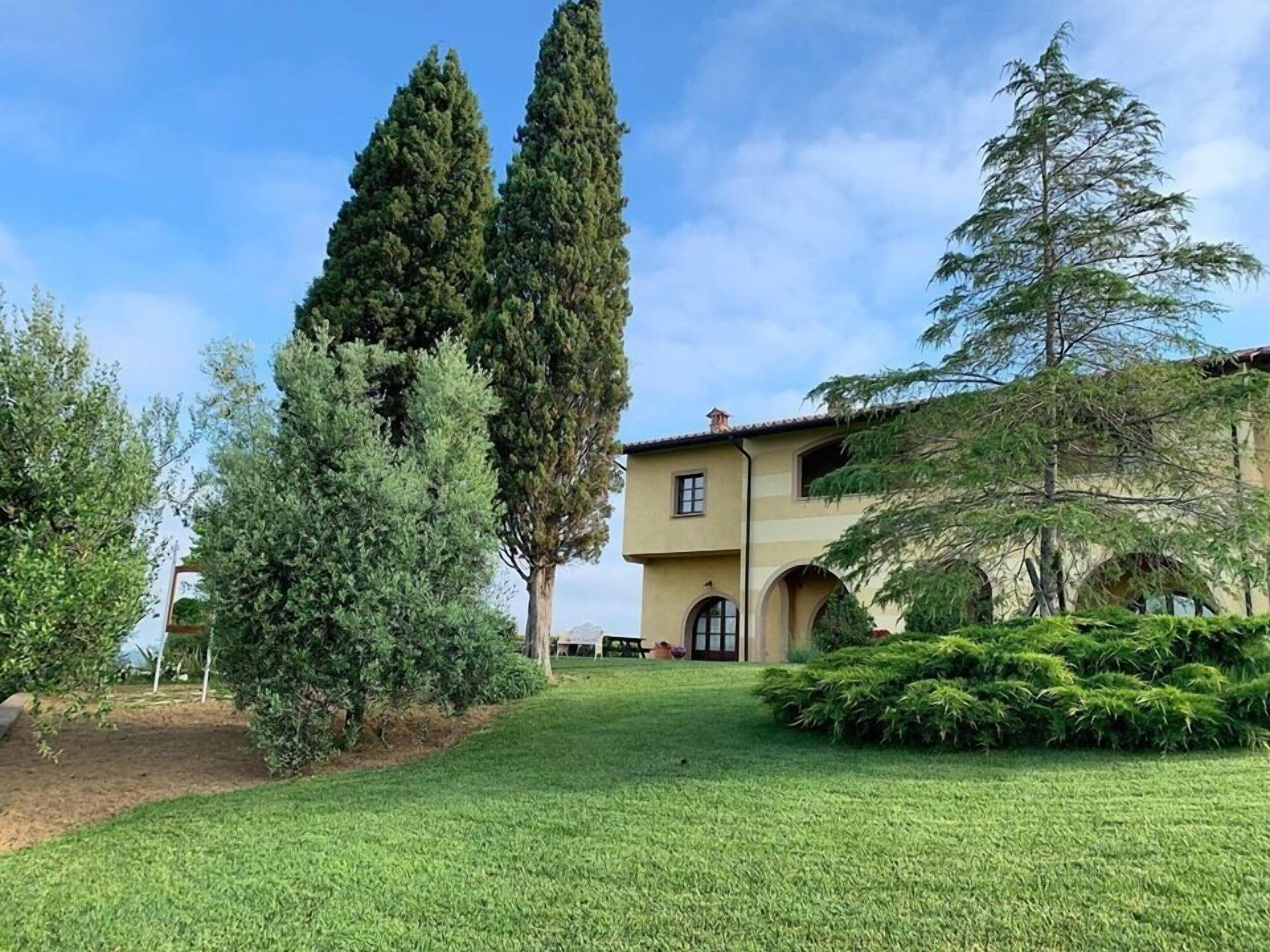 Eine Villa mit gepflegtem Rasen, hohen Bäumen und einem Gebäude im mediterranen Stil.