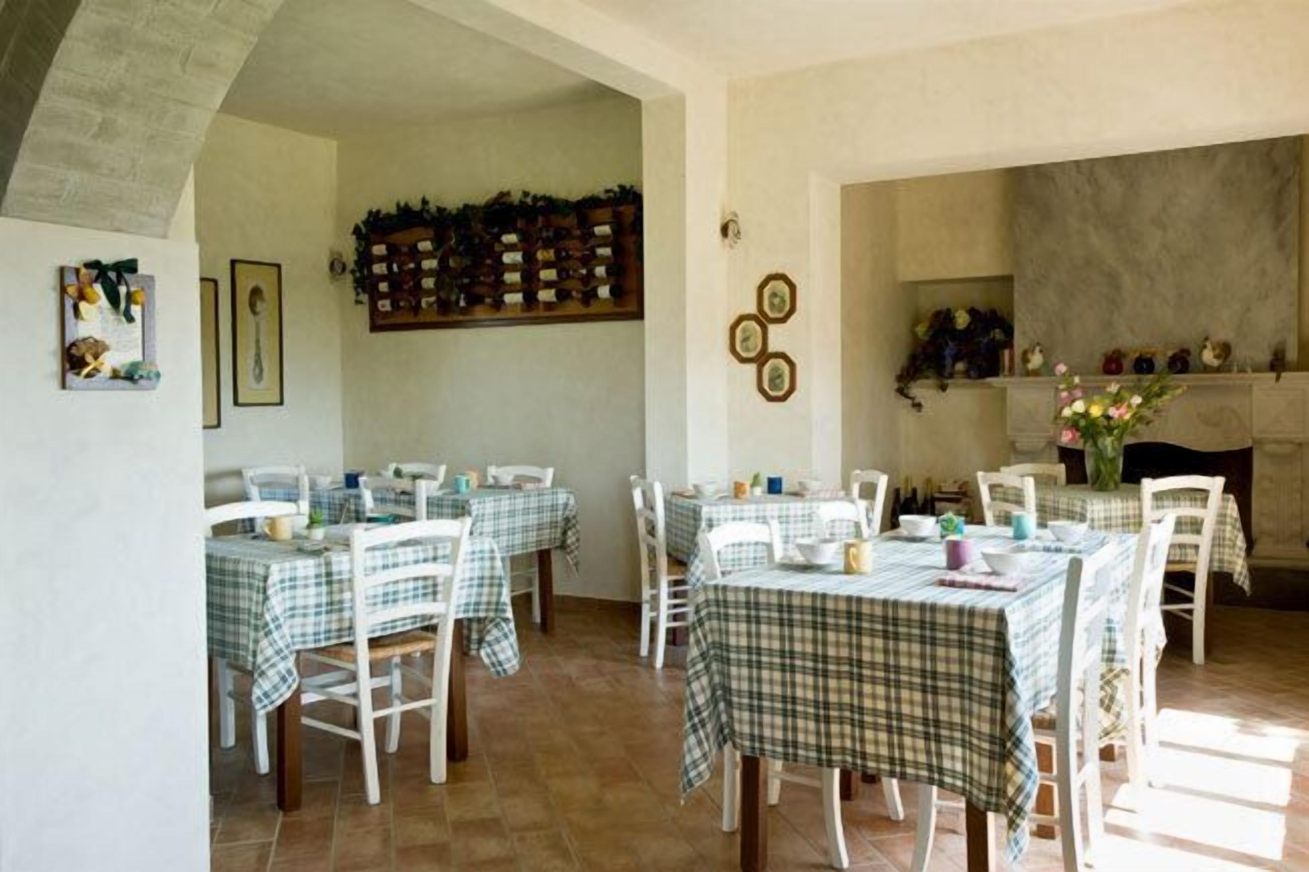 Un comedor con varias mesas cubiertas con manteles a cuadros, sillas blancas y una chimenea al fondo.