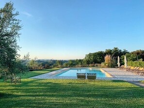 A rectangular swimming pool with a paved deck, surrounded by a well-maintained lawn and a row of lounge chairs. - Agriturismo L'Antica Fornace (Peccioli)