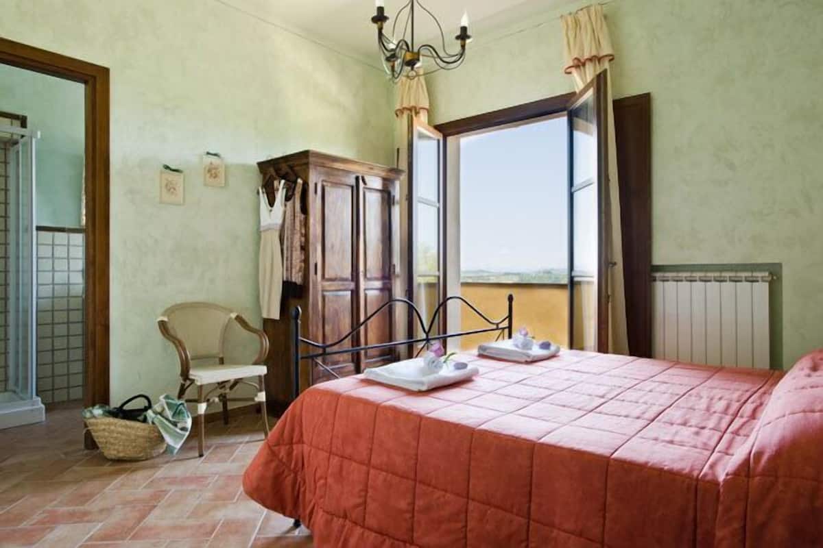 A bedroom with a bed, a wooden wardrobe, a chair, and a window with a view.