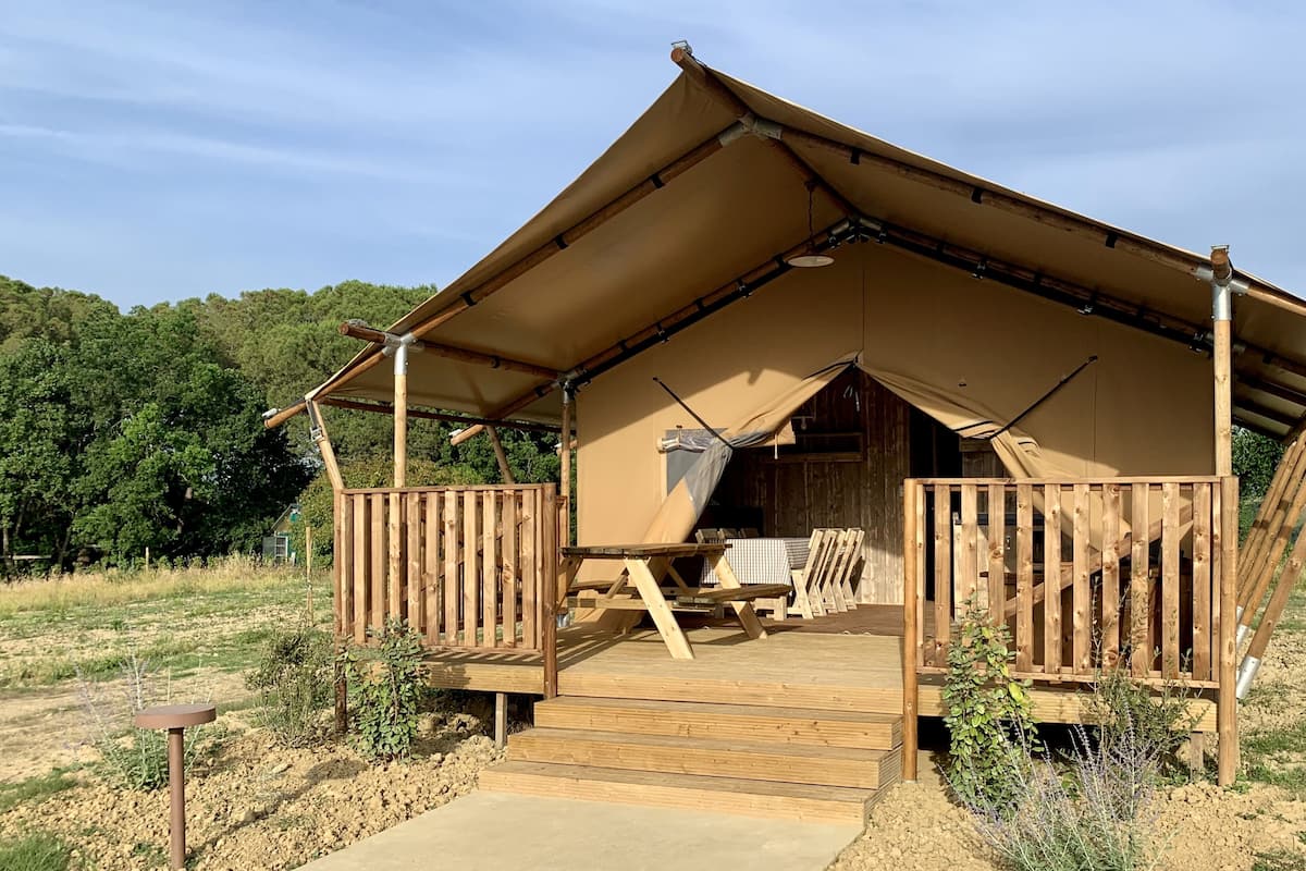 A rustic tent-style accommodation with a wooden deck, a covered entrance, and a view of the surrounding landscape.