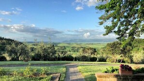 Un sendero serpentea por un exuberante jardín, con vistas a colinas ondulantes y montañas distantes.