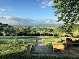 Uma trilha serpenteia por um jardim exuberante, com vista para colinas ondulantes e montanhas ao longe.