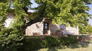 Una casa de piedra con un gran árbol en frente, un jardín cubierto de césped y un muro de piedra.