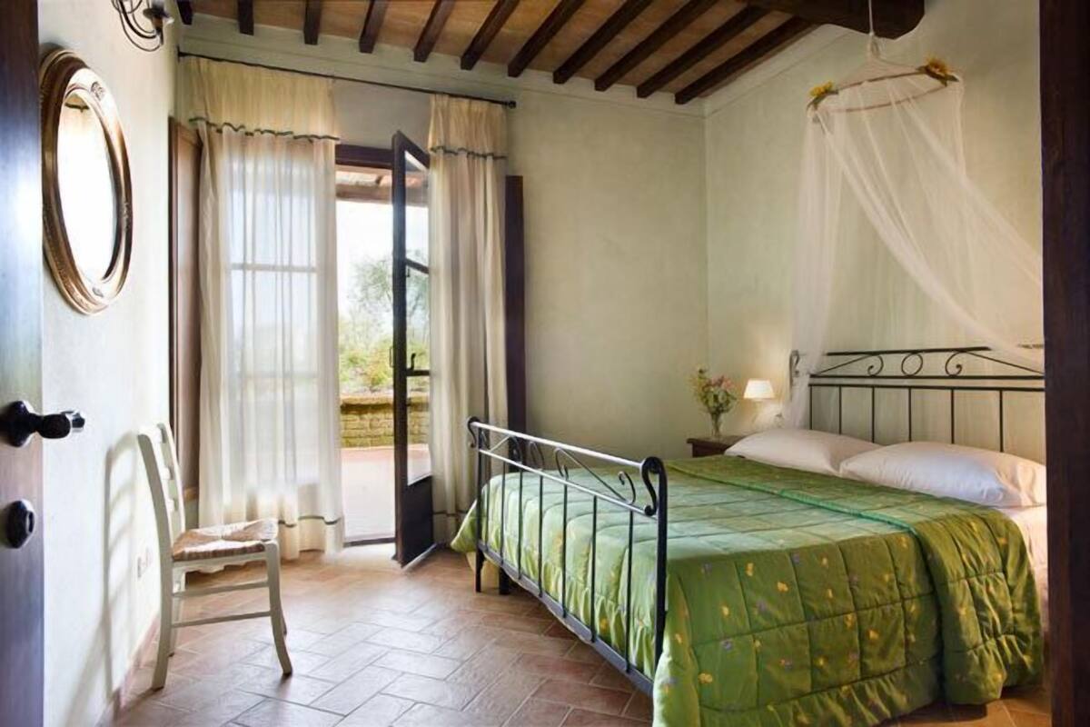 A bedroom with a bed, a chair, a window with curtains, and a door.