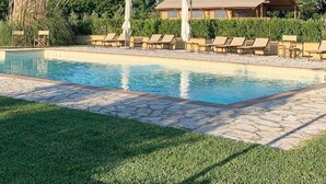 Zona de piscina con sillones de descanso y un edificio al fondo.