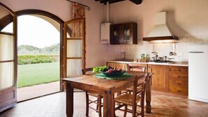Una cocina rústica con armarios de madera, una mesa de comedor con sillas y vistas a un paisaje verde a través de un arco abierto.