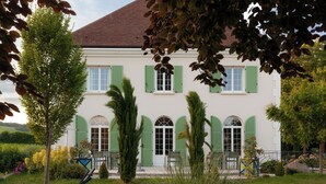 A two-story building with green shutters, a white facade, and a red roof.