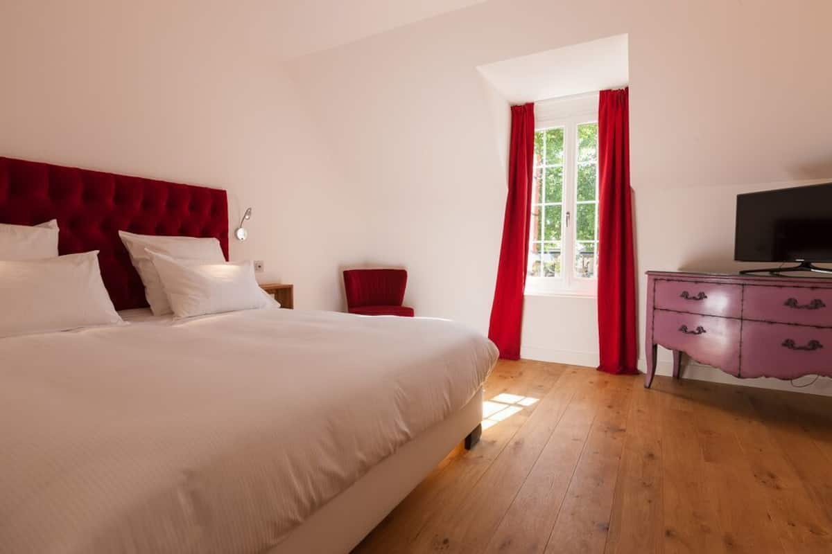 Un dormitorio con una cama grande, una silla roja, un tocador y un televisor.