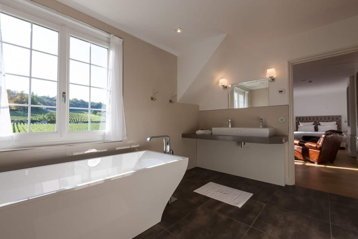 Un baño moderno con una bañera grande, un lavabo doble y un amplio ventanal con vistas a un paisaje verde.