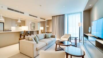 A modern hotel room with a sofa set, a coffee table, a TV, and a large window with curtains.
