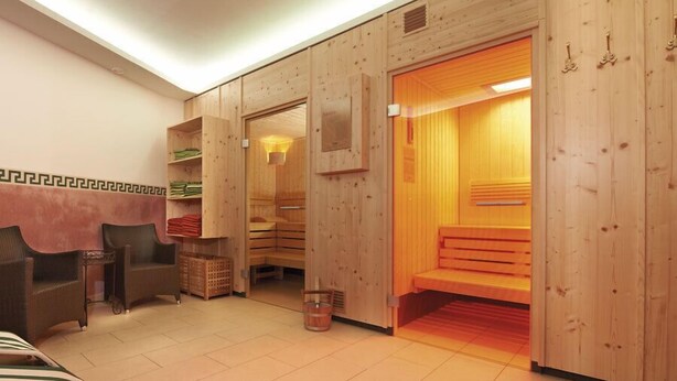 A sauna room with wooden walls, a bench, and a small table with a basket. - Hotel Peter (Saalbach-Hinterglemm)