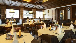 A restaurant with multiple tables set with white napkins, candles, and small vases. - Hotel Peter (Saalbach-Hinterglemm)