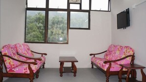 Quarto com duas sofás de madeira com estofamento floral, uma mesa de madeira pequena e uma janela grande com vários painéis que dão para o verde lá fora.