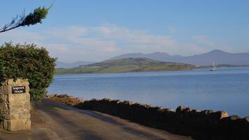 A coastal road leading to Seapoint House with a stone sign, a stone wall, and a view of the sea and distant hills.